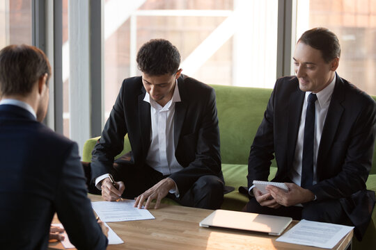 Millennial businessmen make agreement sign contract in office after successful negotiations, satisfied business partners put signature on paper closing deal after briefing. Cooperation concept
