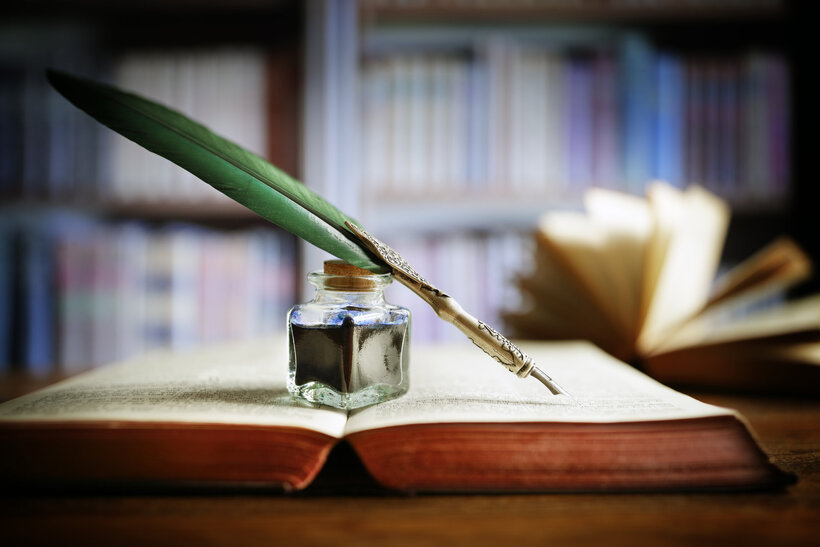 Quill pen and ink well resting on an old book in a library concept for literature, writing, author and history